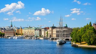 Stockholm's Gamla Stan waterfront with ochre facades, Riddarholmen spire and a moored tall ship under blue sky