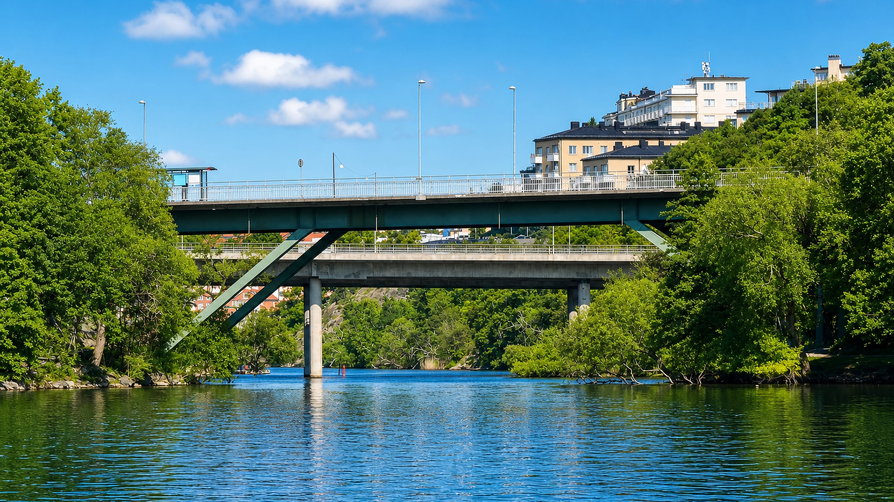 Two low bridges spanning a tree-lined waterway below hillside apartment blocks at Marieberg, Stockholm.