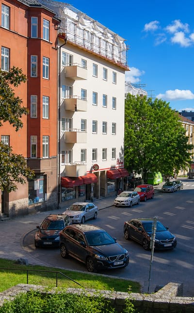 Sundbyberg street lined with red and ochre apartment blocks, parked cars and distant glass towers