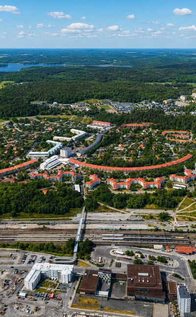 Aerial view of Upplands Vasby's curved orange-roofed housing blocks, rail yard, forests and lakes
