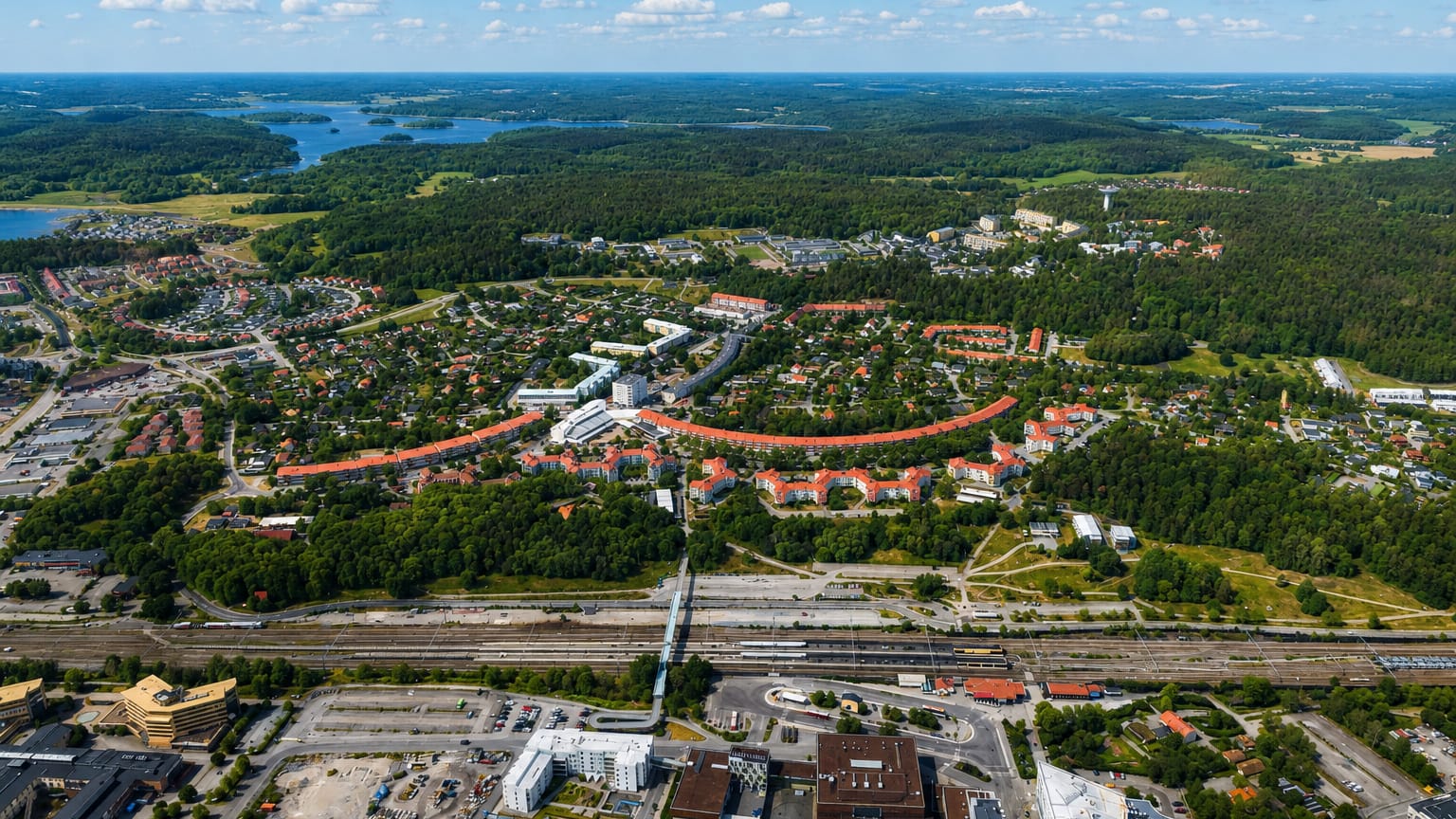 Aerial view of Upplands Vasby's curved orange-roofed housing blocks, rail yard, forests and lakes
