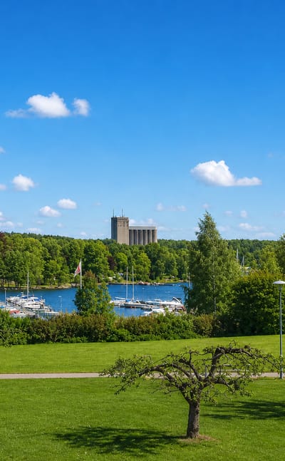 Bålsta, Sweden, from a lakeside park, with a marina of sailboats, a red-and-white tower and a tall concrete silo across the water.