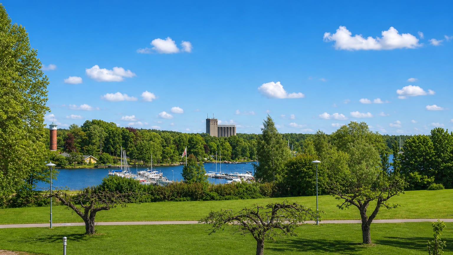 Bålsta, Sweden, from a lakeside park, with a marina of sailboats, a red-and-white tower and a tall concrete silo across the water.