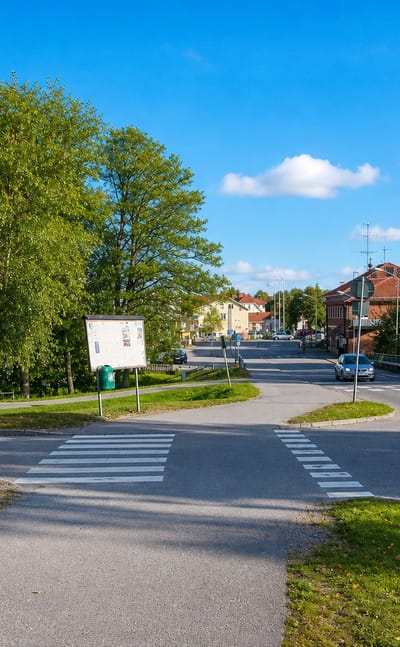 A road junction with a pedestrian crossing, yellow apartment block and birch trees in Heby, Sweden.