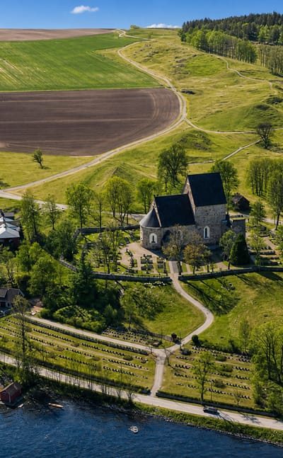 Aerial view of Gamla Uppsala's medieval stone church and walled graveyard amid green fields and forest, Sweden