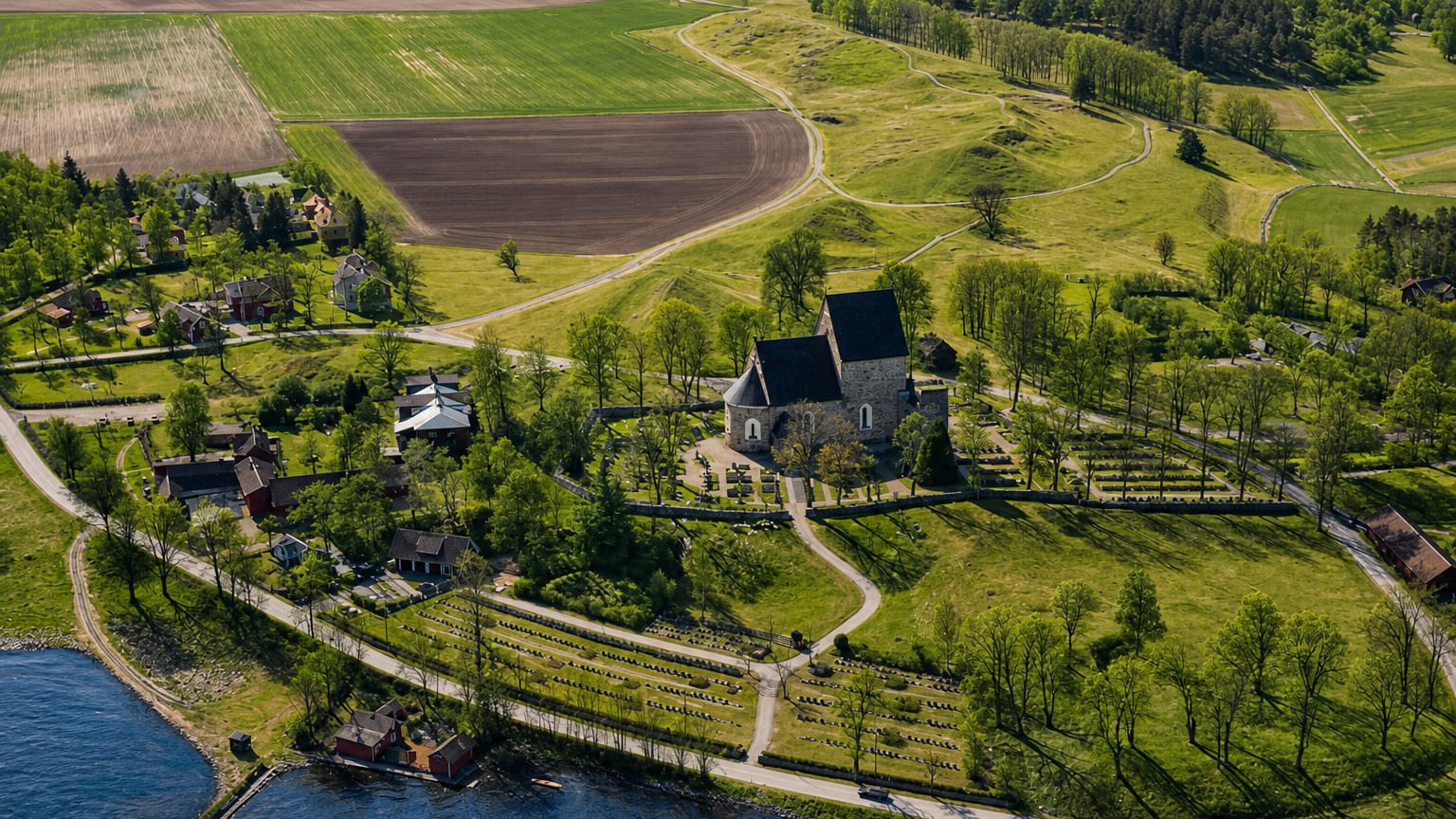 Aerial view of Gamla Uppsala's medieval stone church and walled graveyard amid green fields and forest, Sweden