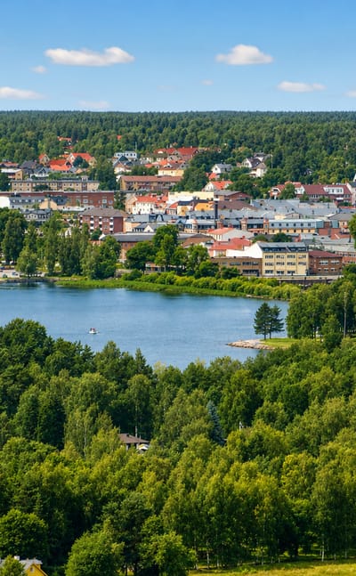 Arvika, Sweden, its red and ochre town centre set on a lake and surrounded by dense green forest under a summer sky.