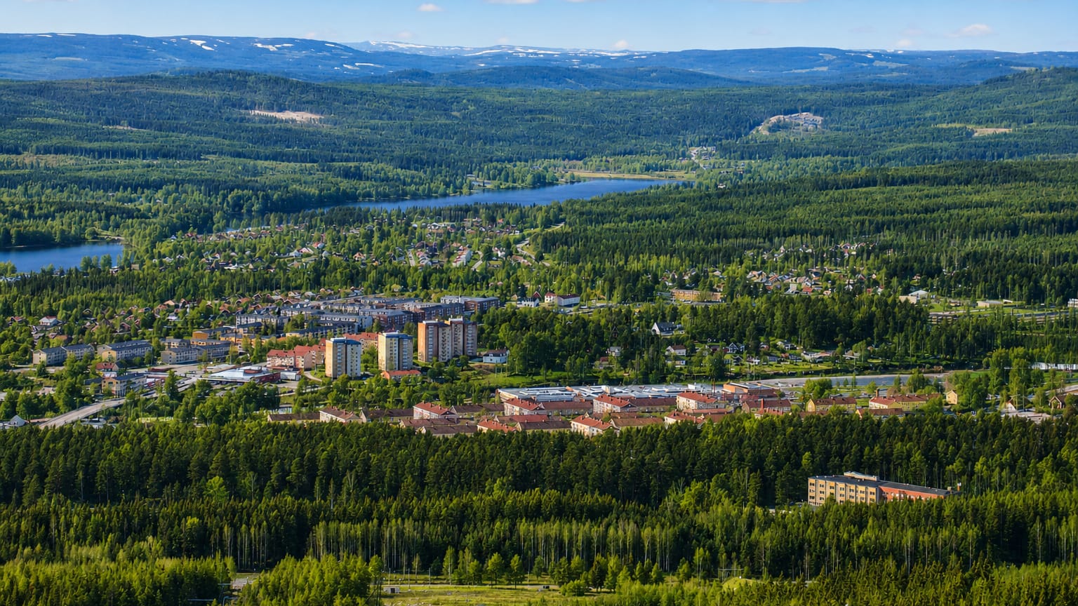 Hagfors nestled among forested hills and lakes with distant snow-capped fells in Värmland, Sweden.