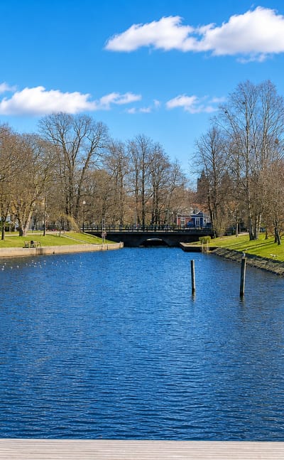 The Varnan river running through Kristinehamn, Sweden, past bare-branched trees and waterfront buildings in spring.