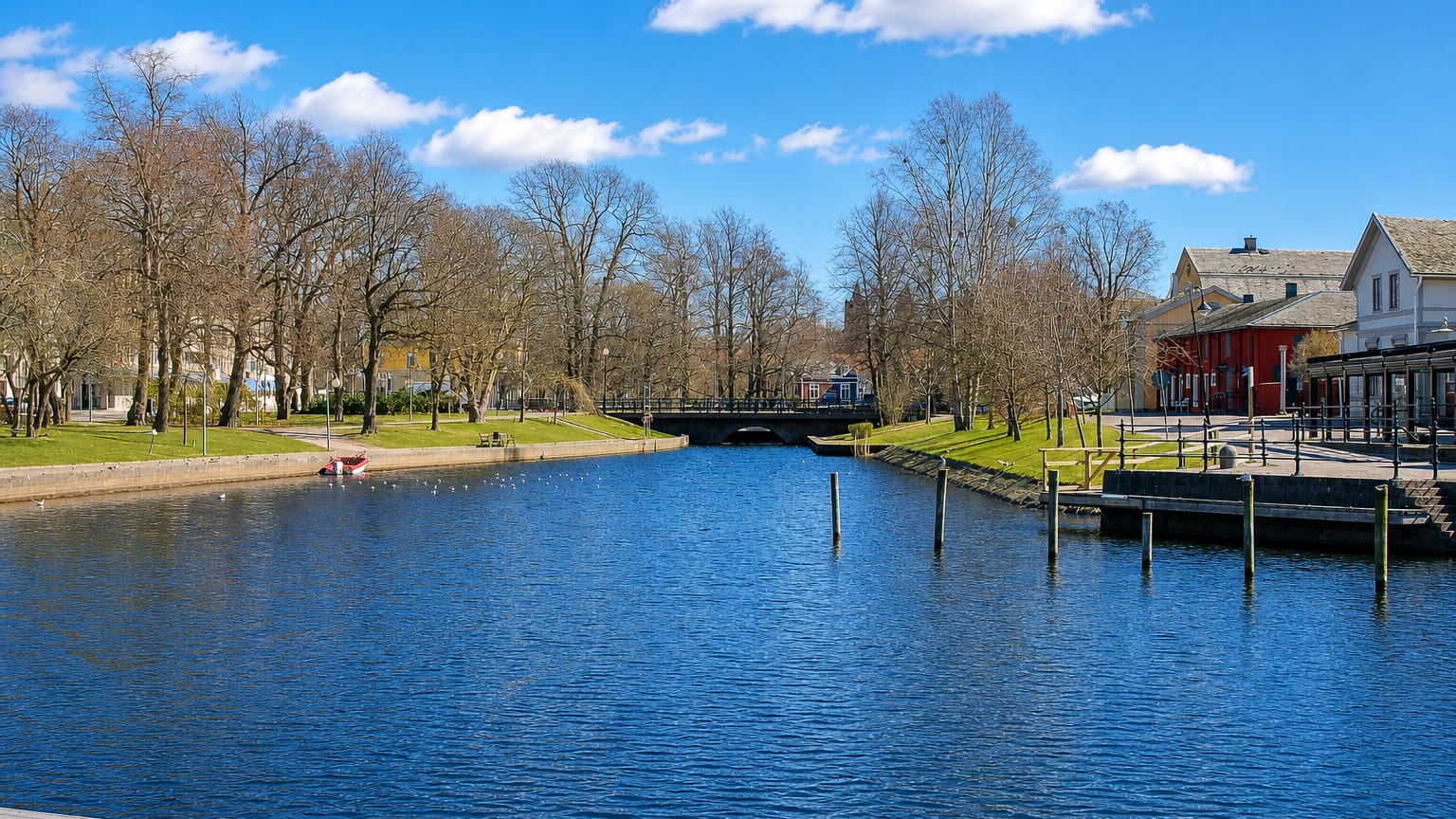 The Varnan river running through Kristinehamn, Sweden, past bare-branched trees and waterfront buildings in spring.