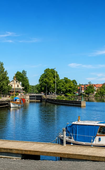 Waterfront in Saffle, Sweden, with a moored boat, a canal lock and an ivy-clad brick building along the river.