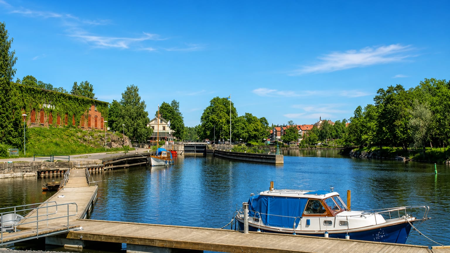 Waterfront in Saffle, Sweden, with a moored boat, a canal lock and an ivy-clad brick building along the river.