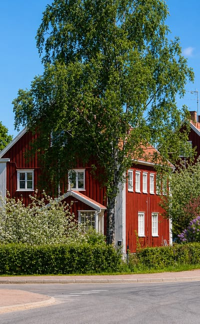 Row of traditional Falu-red wooden houses with white trim along a quiet street in Skoghall, Sweden.