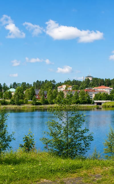 Lycksele's riverside town with a red apartment block and hilltop tower seen across the Ume River in summer.