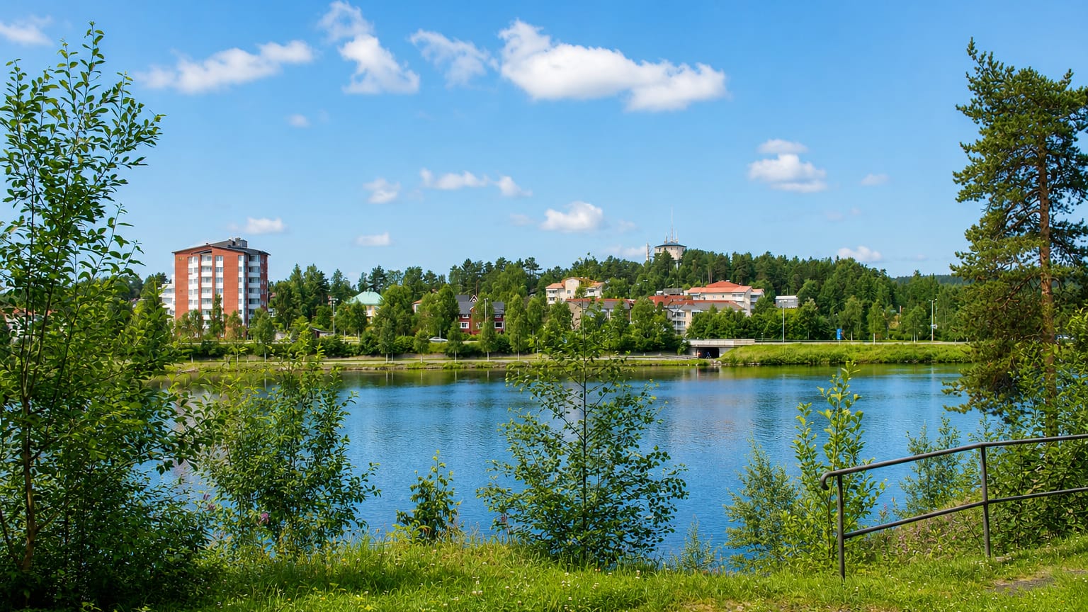 Lycksele's riverside town with a red apartment block and hilltop tower seen across the Ume River in summer.