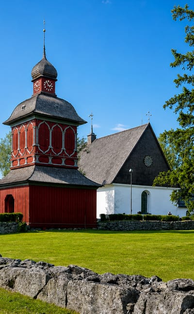 Red timber bell tower beside a white church behind a stone wall in Nordmaling, Sweden.