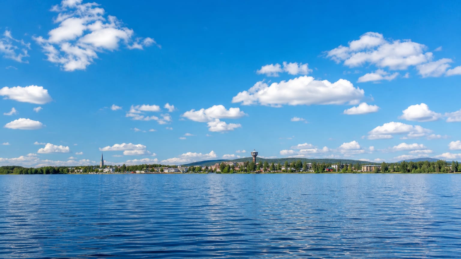 Norsjö, Sweden across the calm lake Norsjön, its church spire and low buildings under a bright blue summer sky