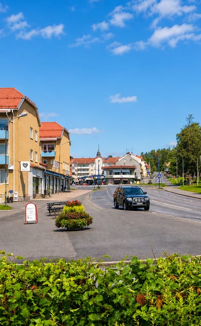 Main-street view with flag-decked shopfronts and a distant church spire in Vilhelmina, Sweden.