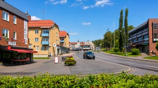 Main-street view with flag-decked shopfronts and a distant church spire in Vilhelmina, Sweden.