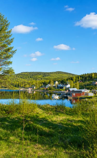 Red cabins along a calm forested lakeshore with wooded hills near Kramfors, Sweden