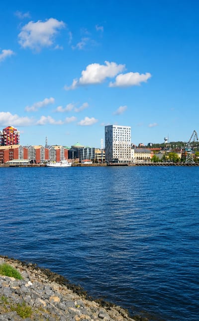 Waterfront skyline of Örnsköldsvik, Sweden, with mid-rise buildings, a church spire and harbour cranes across the bay.