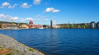 Waterfront skyline of Örnsköldsvik, Sweden, with mid-rise buildings, a church spire and harbour cranes across the bay.
