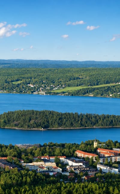 Aerial view of Skönsmon's lakeside apartment blocks among forest, with a wooded island and rolling hills near Sundsvall