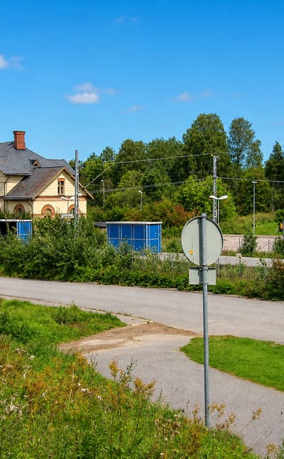 Ornate historic railway station building beside a road and green verges in Hallstahammar, Sweden.