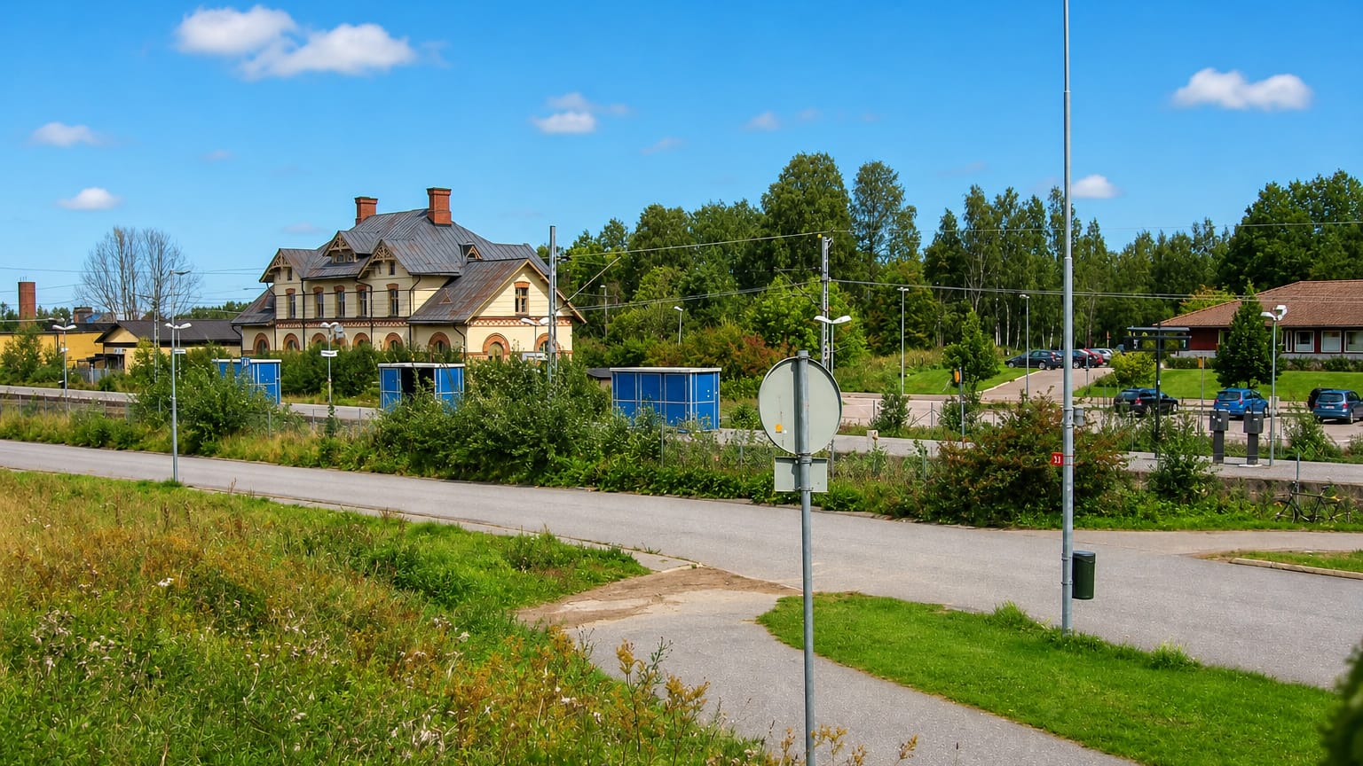 Ornate historic railway station building beside a road and green verges in Hallstahammar, Sweden.