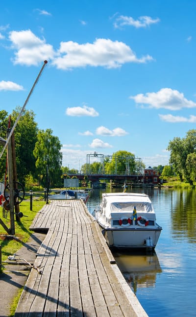 Wooden riverside jetty and boathouse with a moored motorboat and an anchor sign at Kungsör, Sweden