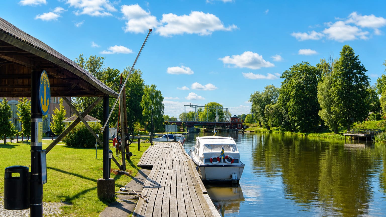 Wooden riverside jetty and boathouse with a moored motorboat and an anchor sign at Kungsör, Sweden