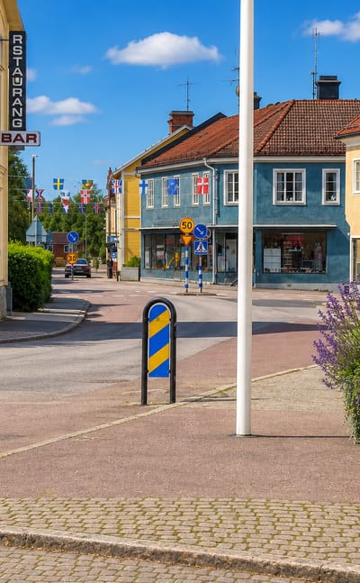 Yellow timber houses, Nordic flag bunting and a flower planter along a cobbled street in Norberg, Sweden.