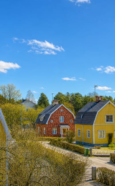Traditional yellow and red wooden houses along a quiet residential street in Surahammar, Sweden, under a blue spring sky.