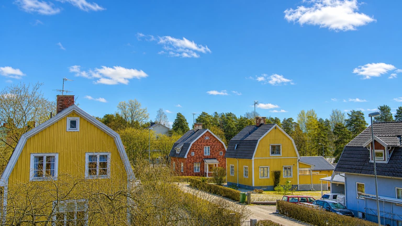Traditional yellow and red wooden houses along a quiet residential street in Surahammar, Sweden, under a blue spring sky.