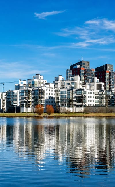 Modern white waterfront apartment blocks of Vasteras reflected in calm Lake Malaren water with a red bridge
