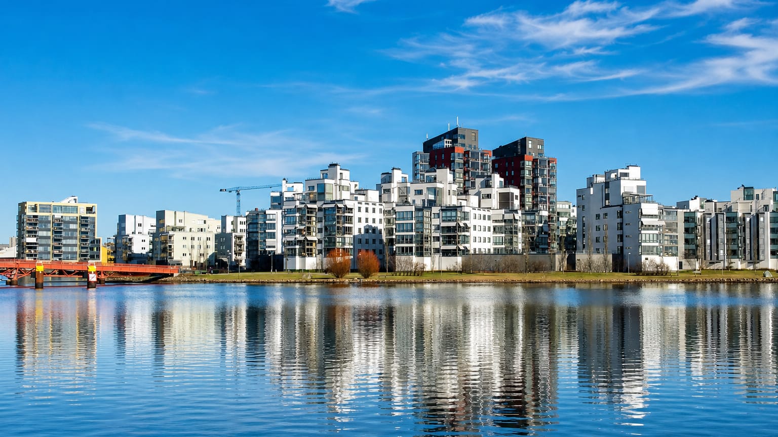 Modern white waterfront apartment blocks of Vasteras reflected in calm Lake Malaren water with a red bridge