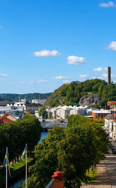 Alingsas townscape with a canal, Swedish flags, brick buildings and a wooded hill, Sweden