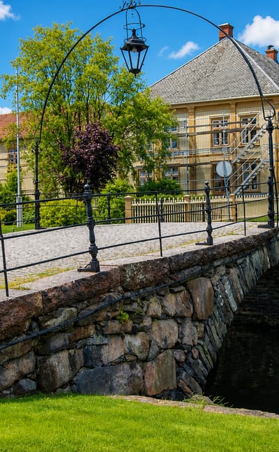 Old stone arch bridge over a canal beside yellow timber houses in Amal, Sweden