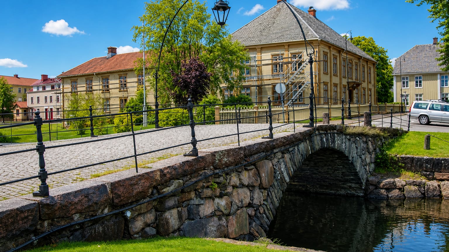 Old stone arch bridge over a canal beside yellow timber houses in Amal, Sweden