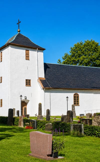 Färgelanda's whitewashed stone church with a dark roof, set in a green churchyard dotted with gravestones.