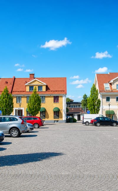 Cobbled town square in Götene, Sweden, framed by yellow and cream buildings with red-tiled roofs.