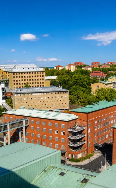 Elevated daytime view over Änggården in Gothenburg, with red brick buildings, green copper roofs and hillside apartment blocks.