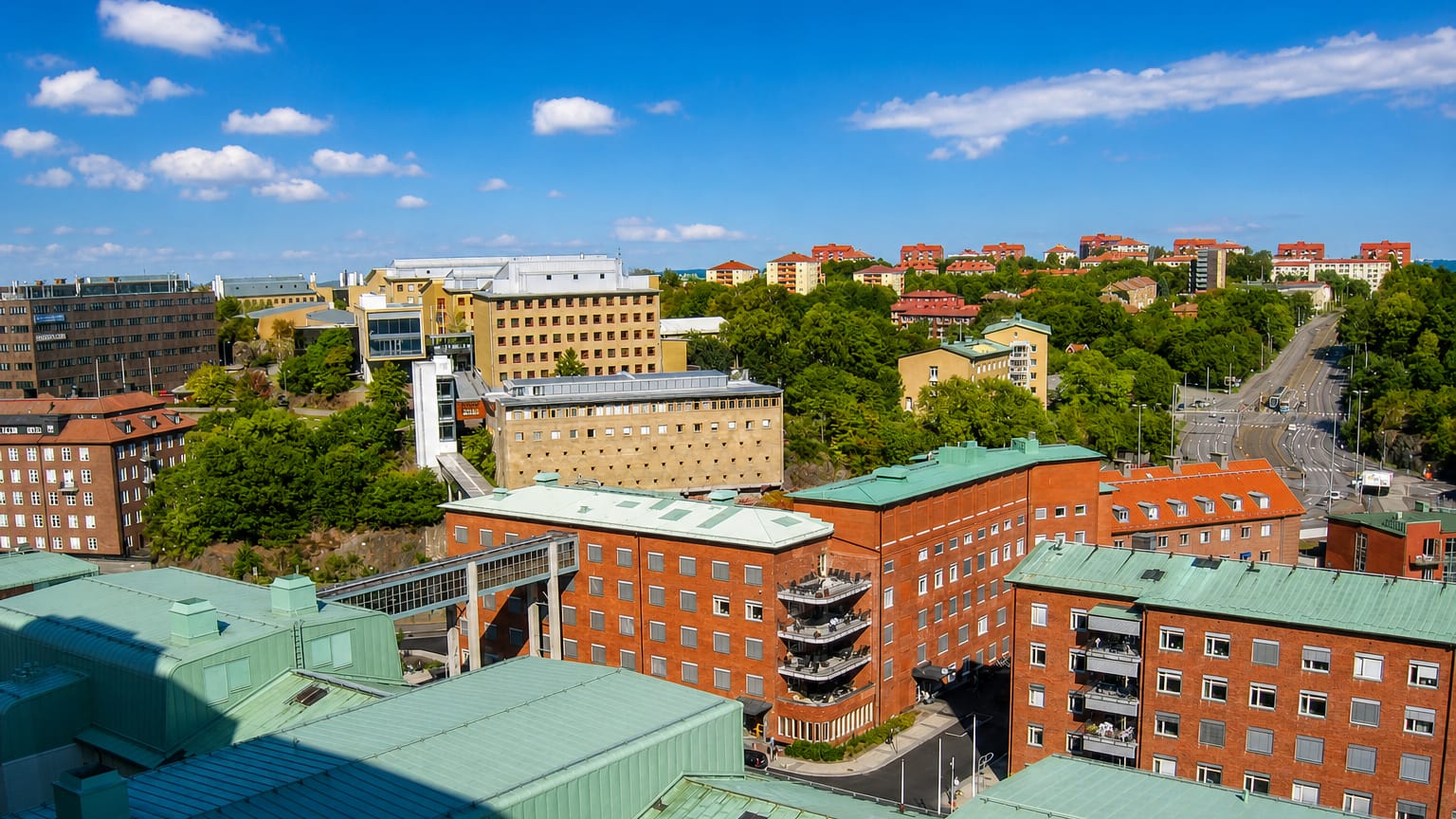Elevated daytime view over Änggården in Gothenburg, with red brick buildings, green copper roofs and hillside apartment blocks.