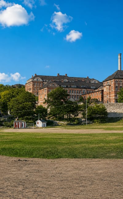 Red-brick Annedalskyrkan church and brick institutional buildings on a green hillside above a parkland field in Annedal, Gothenburg.