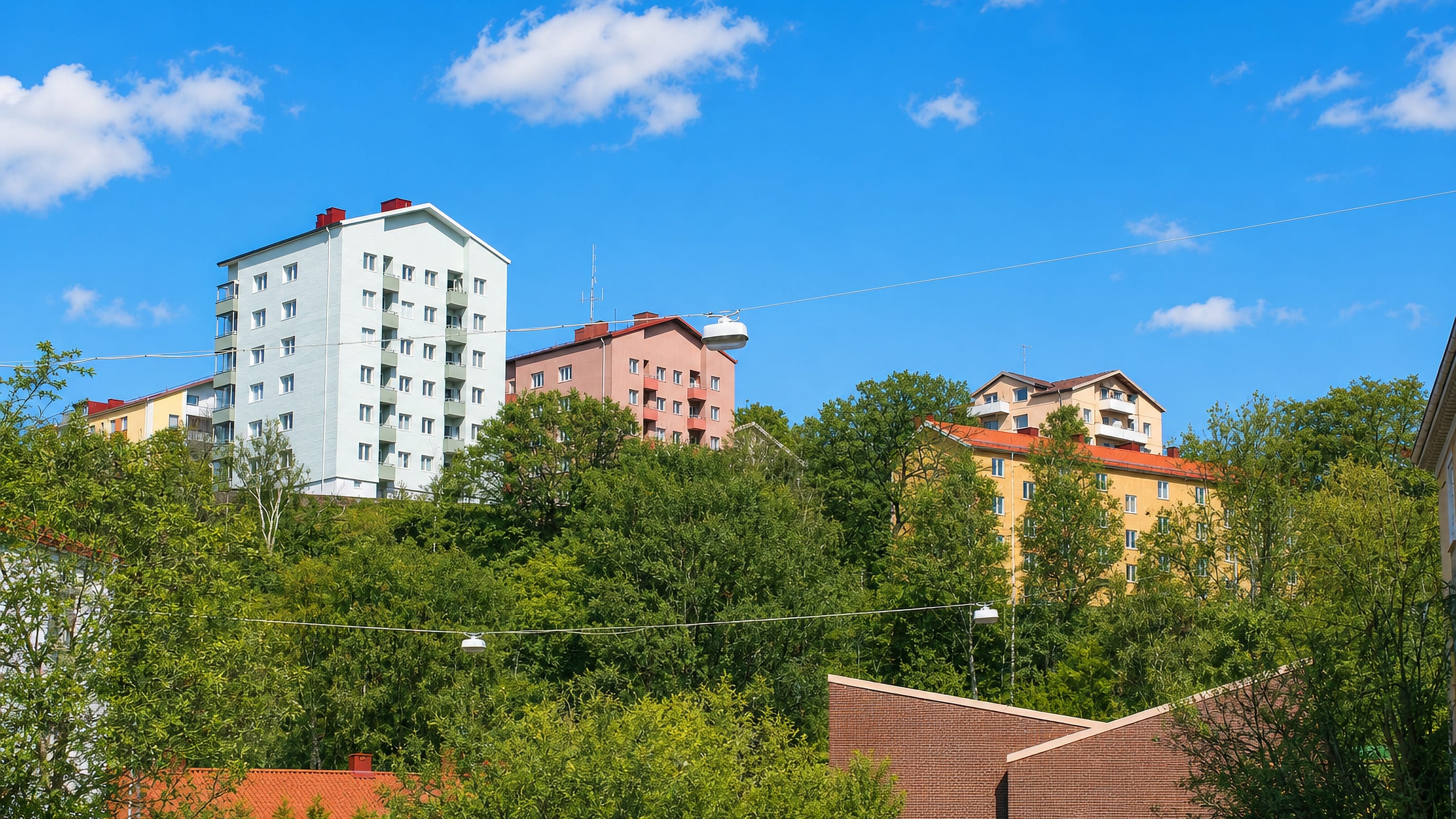 Hillside apartment blocks in white, pink and yellow rising above trees in Bagaregarden, Gothenburg.