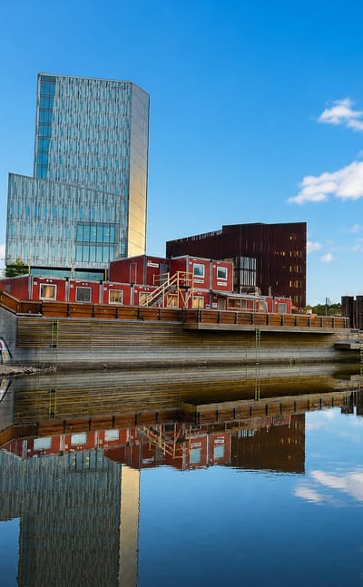 Gamlestaden riverside in Gothenburg with a blue glass high-rise and red-brick industrial buildings reflected in calm water