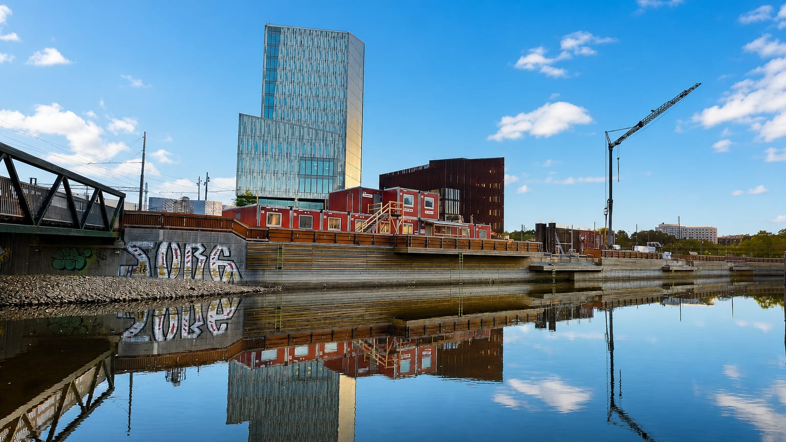 Gamlestaden riverside in Gothenburg with a blue glass high-rise and red-brick industrial buildings reflected in calm water