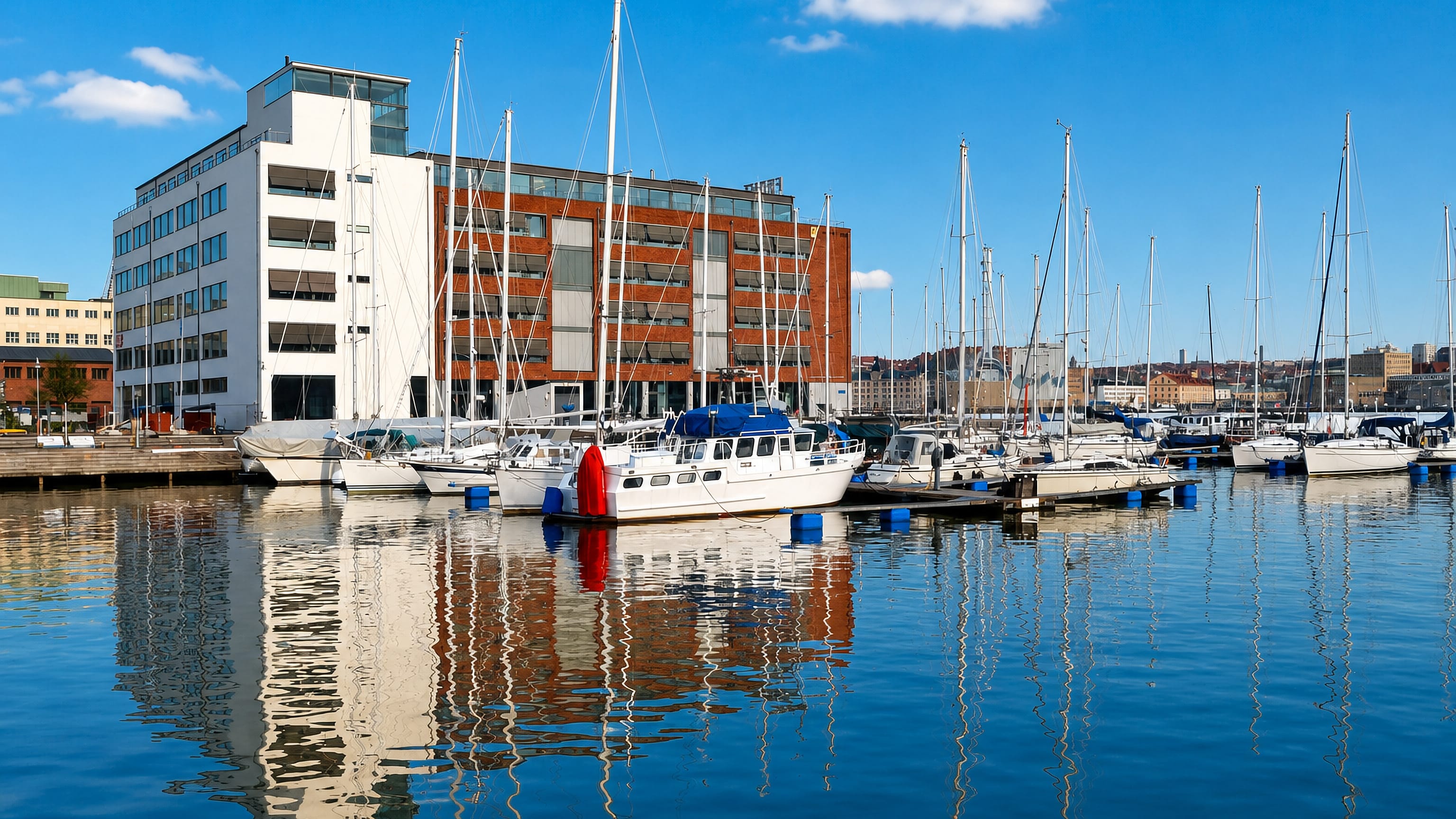 Yachts moored at Lindholmen's marina in Gothenburg below waterfront brick and glass office buildings.