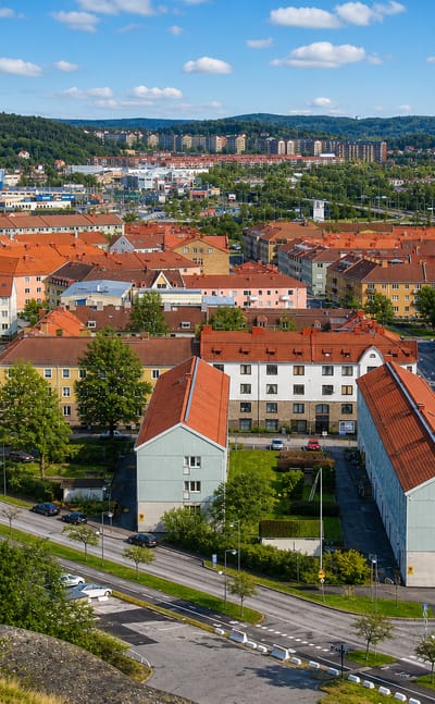 Elevated daytime view over Lundby's red-roofed houses and pastel apartment blocks toward wooded hills, Gothenburg, Sweden