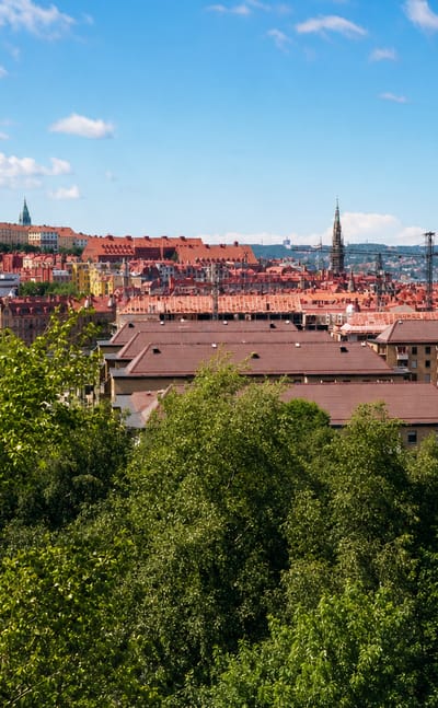 Hilltop view across the red rooftops of Olivedal, Gothenburg, with green treetops, a church spire and a distant bridge.